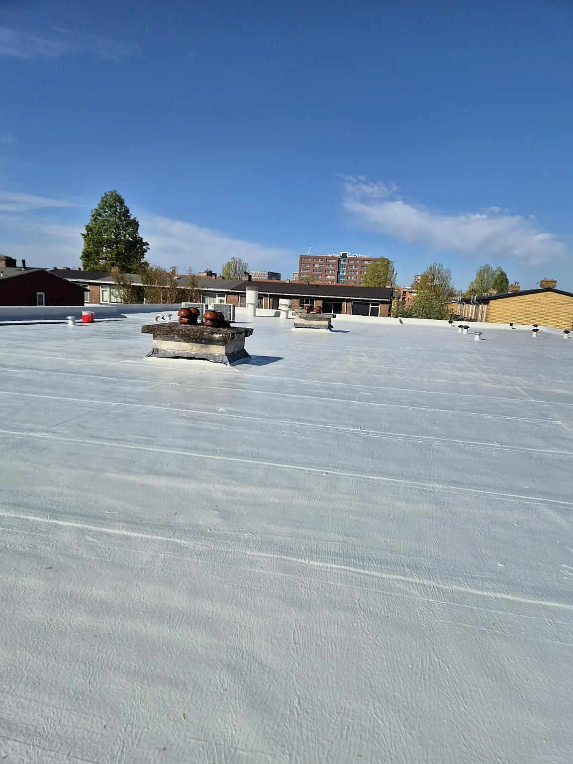 Groot plat dak na renovatie met een wit vloeibaar waterdichtingssysteem